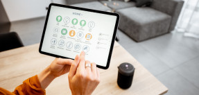 Woman's hands holding up tablet with icons for smart home features 