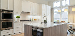 A kitchen with light cabinets and a gray-wood island. Light stone countertops and stainless steel appliances throughout.