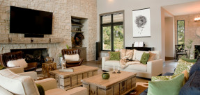 Photo of a modern living room with a mounted flat screen on a rock facade wall and a lot of light-colored furniture