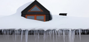 Photo off a roof with an orange-rimmed window covered in snow and icicles