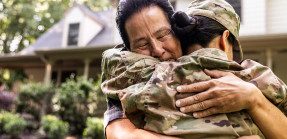 A veteran returns home and embraces their father in a hug outside their home