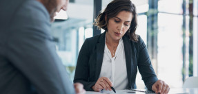 Businesswoman with short brown hair goes over document details with make colleague