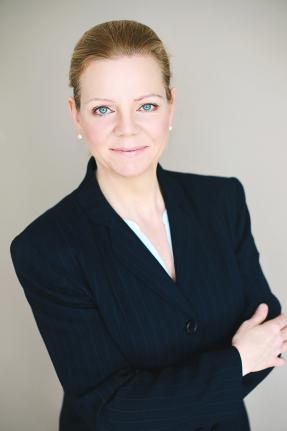 Headshot image of Carolyn Schwaar, facing camera in black jacket with tan background