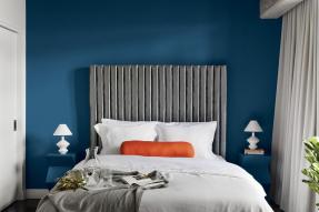 A bedroom, containing a bed with a large headboard against a blue wall, flanked on both sides by blue nightstands