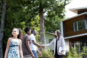 African-American family and real estate agent shaking hands in front of a house