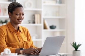 Happy short-haired millennial african american lady freelancer using laptop at home, sitting at workdesk 