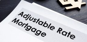 A picture of a document titled "Adjustable-Rate Mortgage" on a table, with a paper cut out of a house next to it out of frame.
