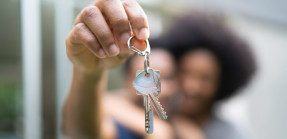 A picture of two Black homeowners holding house keys up close to the camera, blurring their faces in the background.