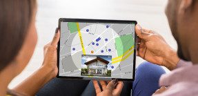A man and a woman look at an online map of house listings on a smart tablet