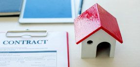 A picture of a house miniature next to a clipboard holding a document titled "Contract."