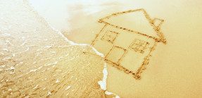 A picture of a house drawn on the beach with the tide approaching about to wash it away.