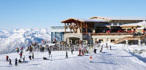 A picture of a ski resort with skiers and other guests in the snow in front of it.