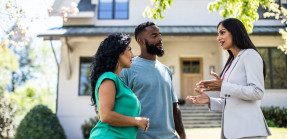 Real estate agents speaking with couple outside a house. 