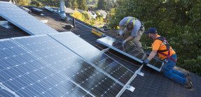 Two men installing solar panels on house roof.