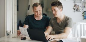 Gay couple completing home closing or financial transaction on laptop computer.