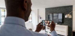 A man touring the inside of a home video chats with two friends on his phone.