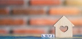 On a table, block letters spelling "LOVE" next to a small abstract house with a heart cut out