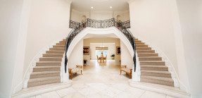A picture of a mansion's interior with two curved staircases on either side of the entrance.