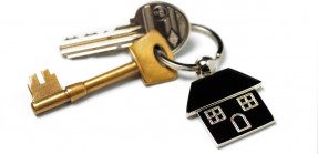 A closeup picture of a set of keys on a ring with a simple house keychain on a white background.