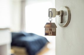 A door opening up to the inside of a home with a key in the lock and a house-shaped keychain hanging down.