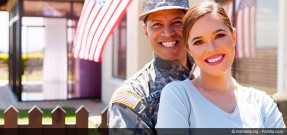 Veteran and spouse smile, embrace in front of home