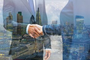 Business handshake superimposed on city skylines