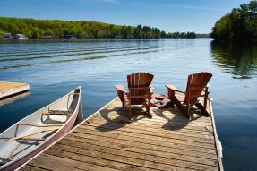Canoe next to dock with two Adirondack chairs