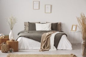 Soft bed with blanket and pillows located near wall with decorations in a white bedroom.