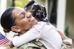 Daughter embracing female soldier mother in front of their house