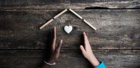 Hand of black and white kids making a house with heart shaped marble