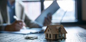House model on table with person looking at contract in background