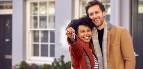 Portrait of smiling couple in front of home holding keys
