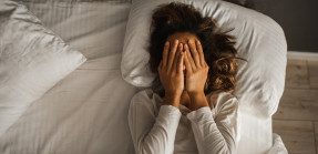 Woman laying in bed with hands over her face