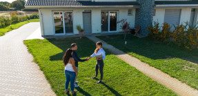 Youn couple shaking real estate agent's hand in front of home