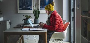 Man working at home in puffer coat and winter hat