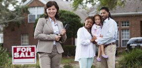 Real estate agent with family in front of house with for sale sign