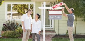 Real estate agent hanging a sold sign in front of house