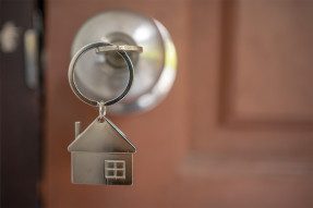 House-shaped keychain with key in front door lock
