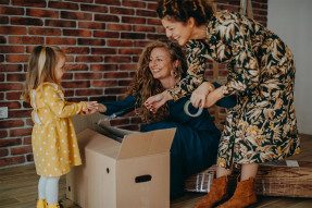 Little girl with two moms unpacking boxes in home