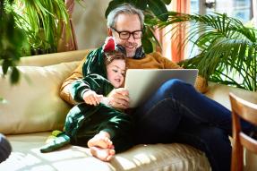 Middle-aged man and a child sitting on a couch and looking at a laptop