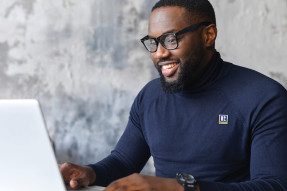 Man with R badge smiling at laptop