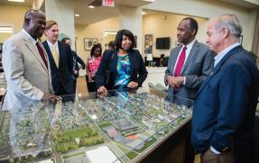 HUD Secretary Ben Carson surrounded by four people standing next to a scaled down community housing plan display