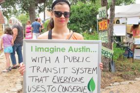 A woman holding up a sign that says "Imagine Austin with a public transportation system that everyone uses, to conserve"