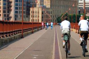 Two men riding a bicycle over a pedestrian bridge in downtown Minneapolis
