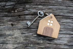 Old-fashioned key with wooden house keychain on weathered gray board