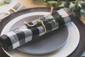 A plaid napkin sitting on top of a gray plate and white with black rim charger