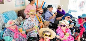 A group of seniors in festive hats, sunglasses, Hawaiian shirts and leis enjoying beverages