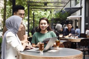 Professional woman and two clients looking at a laptop in a sidewalk cafe
