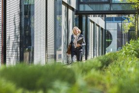 Professional woman walking between an office building and a garden