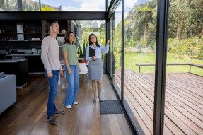 Real estate agent showing clients a modern home with a glass wall and wooden deck